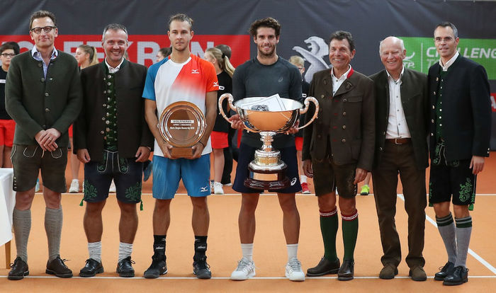 Die Gewinner des Wolffkran Opens die mit den Pokalen in der Mitte stehen. Zu beiden seiten stehen zum einen Personen des Bayerischen Tennisverbandes, als auch Dr. Peter Schiefer von Wolffkran. Alle, außer die Tennisspieler, haben Lederhosen an.