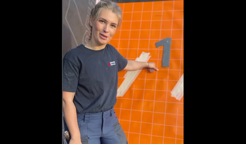 Dachdeckerin Chiara steht vor einer orangenen Wand, auf die sie eine "1" montiert hat. Die Nummer steht für die Rückennummer vom nominierten Torwart Manuel Neuer
